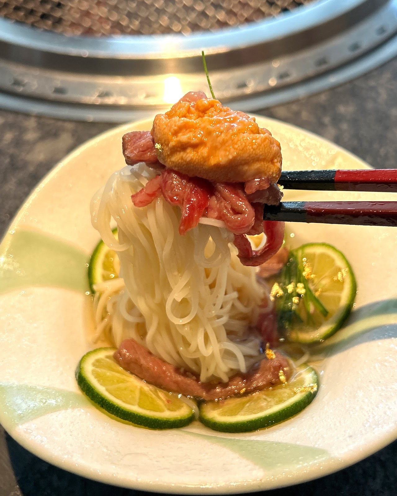 ウニと生の牛肉をのせた細い麺を箸で持ち上げたところ。