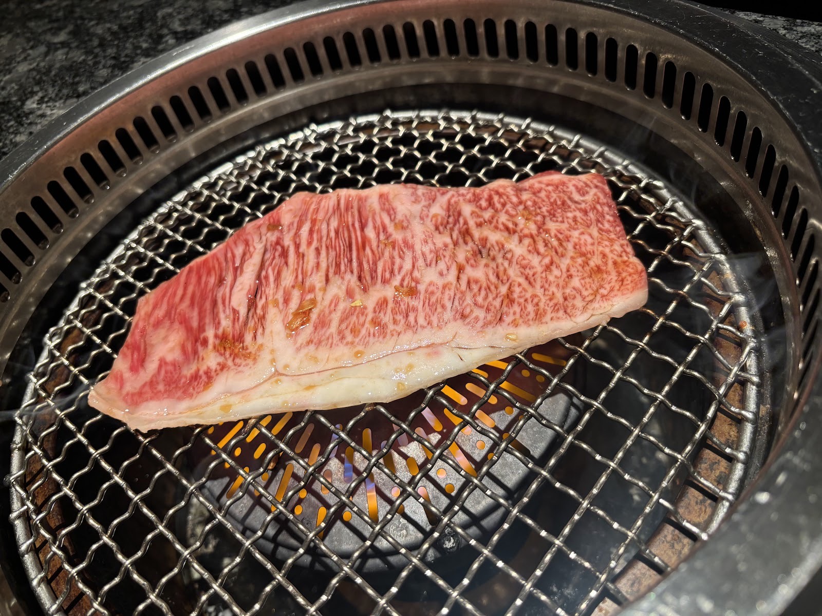 丸い焼き網の上で焼かれる霜降り肉の厚切り。網の下に炎。
