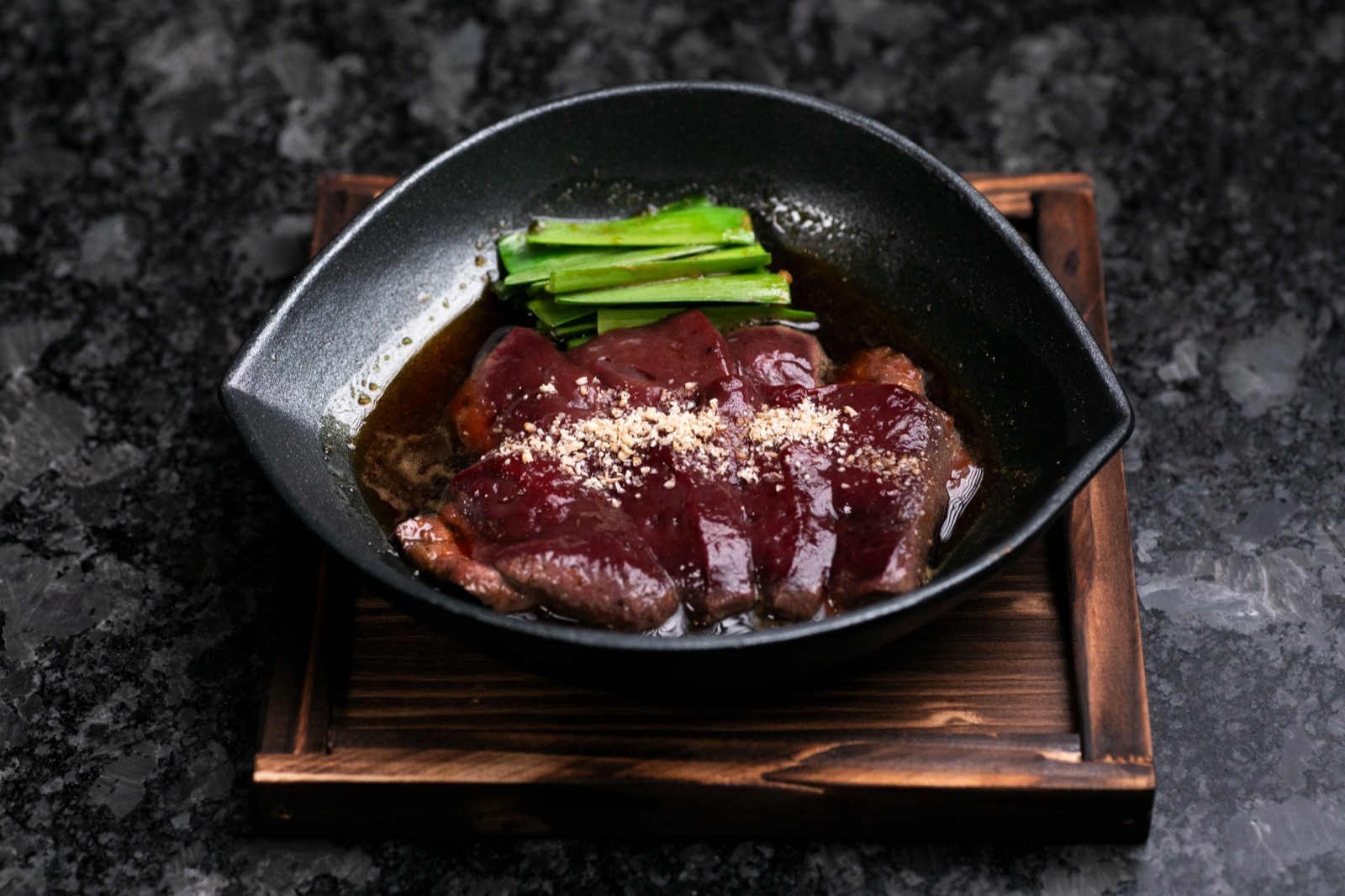 木の台にのせた黒い器に、たれをからめた艶のある赤黒い肉の薄切りとにら。